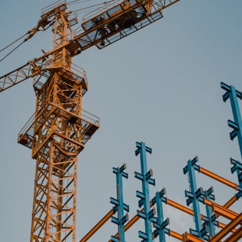 Top of an orange crane working on constructing orange and blue beams of a new building